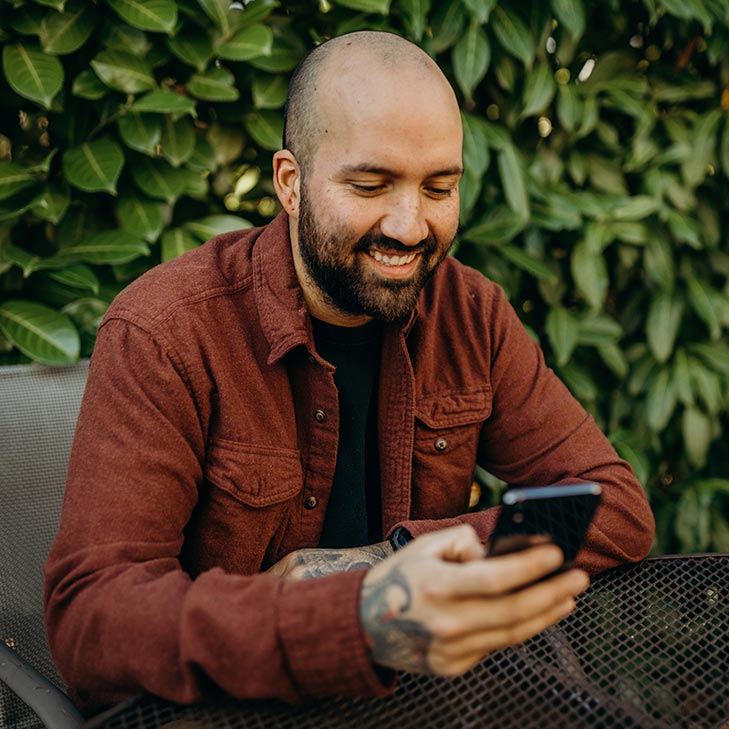 Man with phone sitting at a table outside